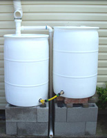 Two White Rain Barrels Connected on Concrete Block Stand